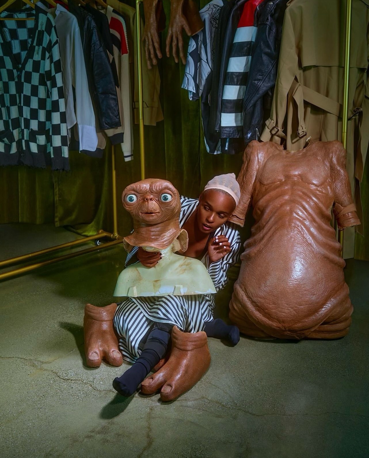 Creative studio shot featuring a Black female in a striped shirt next to an E.T. the Extra-Terrestrial prop and clothing rack.