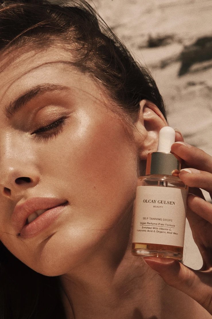 Close-up shot of a woman holding an Olcay Gulsen Beauty serum bottle, showcasing skincare and beauty in a sunlit outdoor setting.
