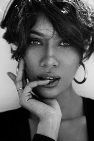 Close-up monochrome portrait of a woman with short dark hair, hoop earrings, and hand near her face.