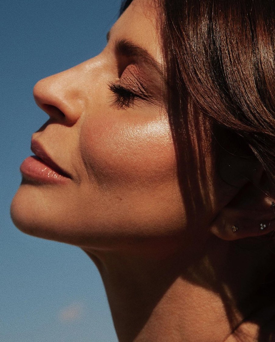 Close-up studio portrait of an adult female with brown hair and fair skin, gazing upward against a clear blue sky.