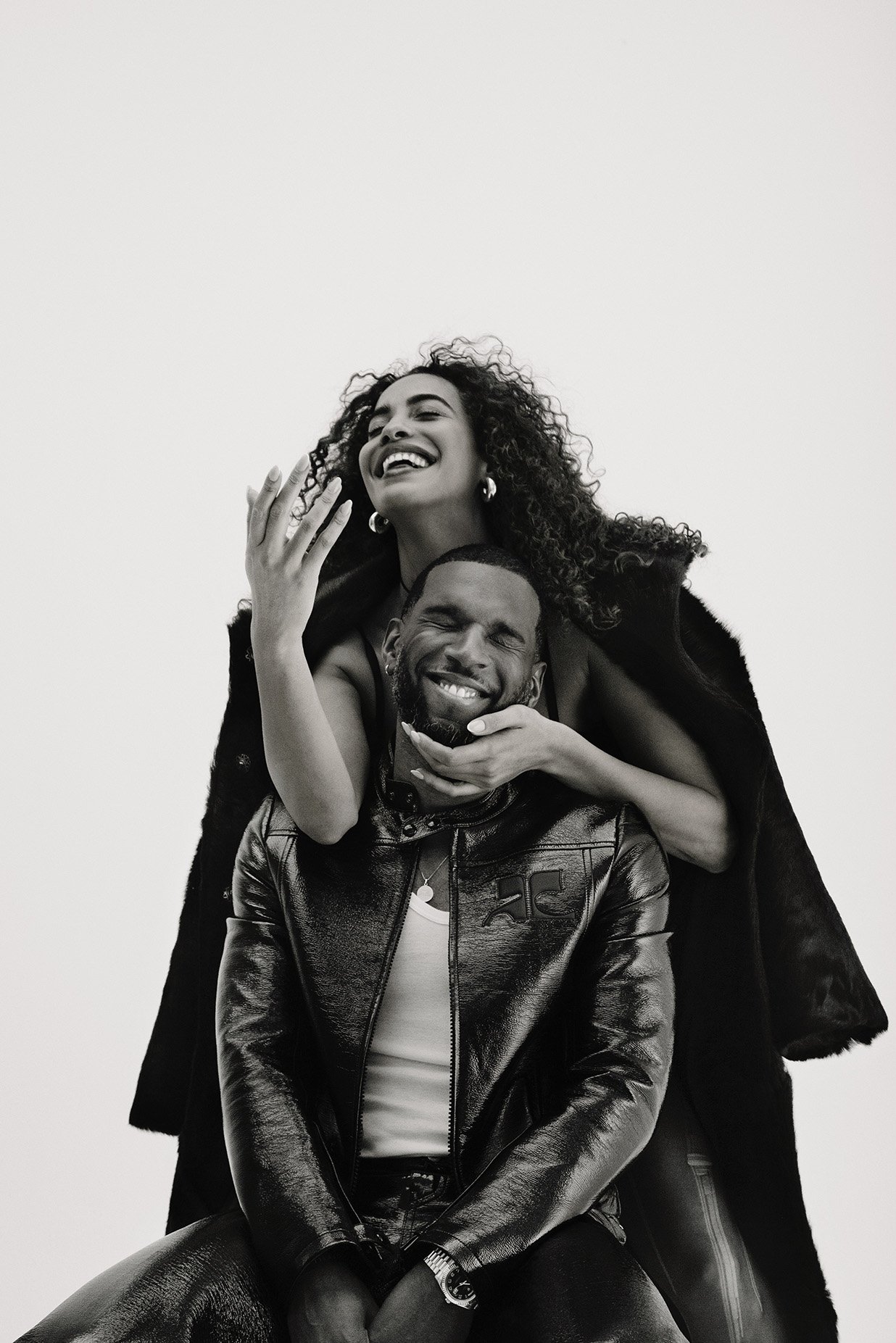 Black and white shot of an African American couple: a woman with curly hair stands behind a seated man in a jacket, both smiling.