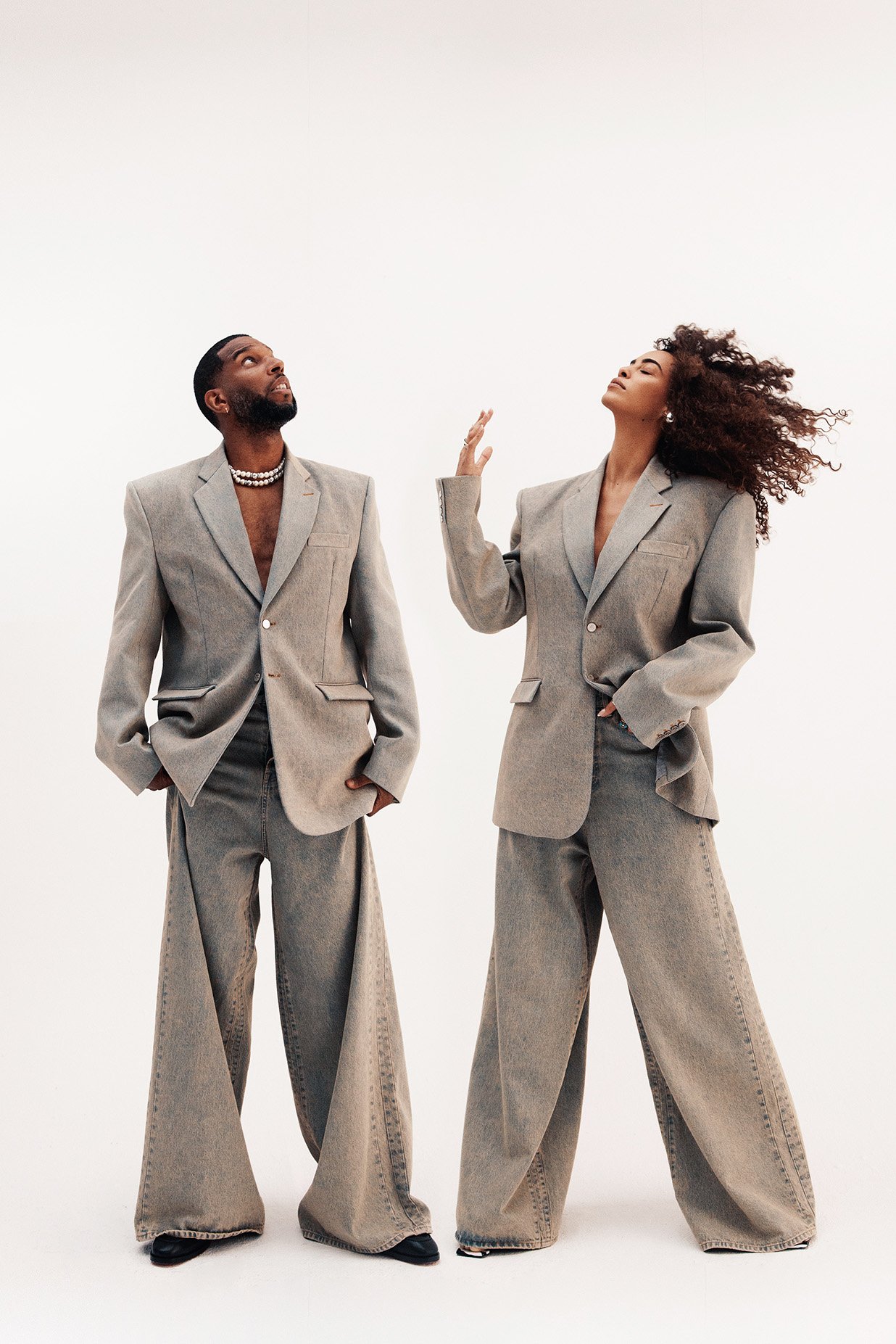 Two models wearing oversized grey blazers and matching wide-leg trousers posing against a plain white background