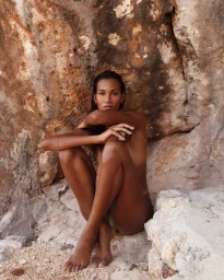 Black woman seated against a rocky cliff face outdoors holding a glass jar