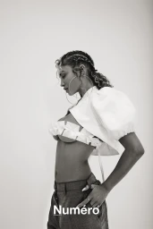 Black and white portrait of a woman wearing a white cropped top with puff sleeves and dark trousers against a plain background