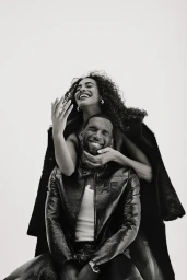 Black and white portrait of a smiling man and laughing woman posing together against a bright white background