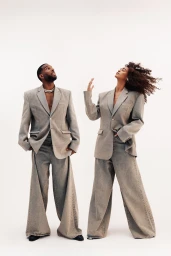 Two models wearing oversized grey blazers and matching wide-leg trousers posing against a plain white background
