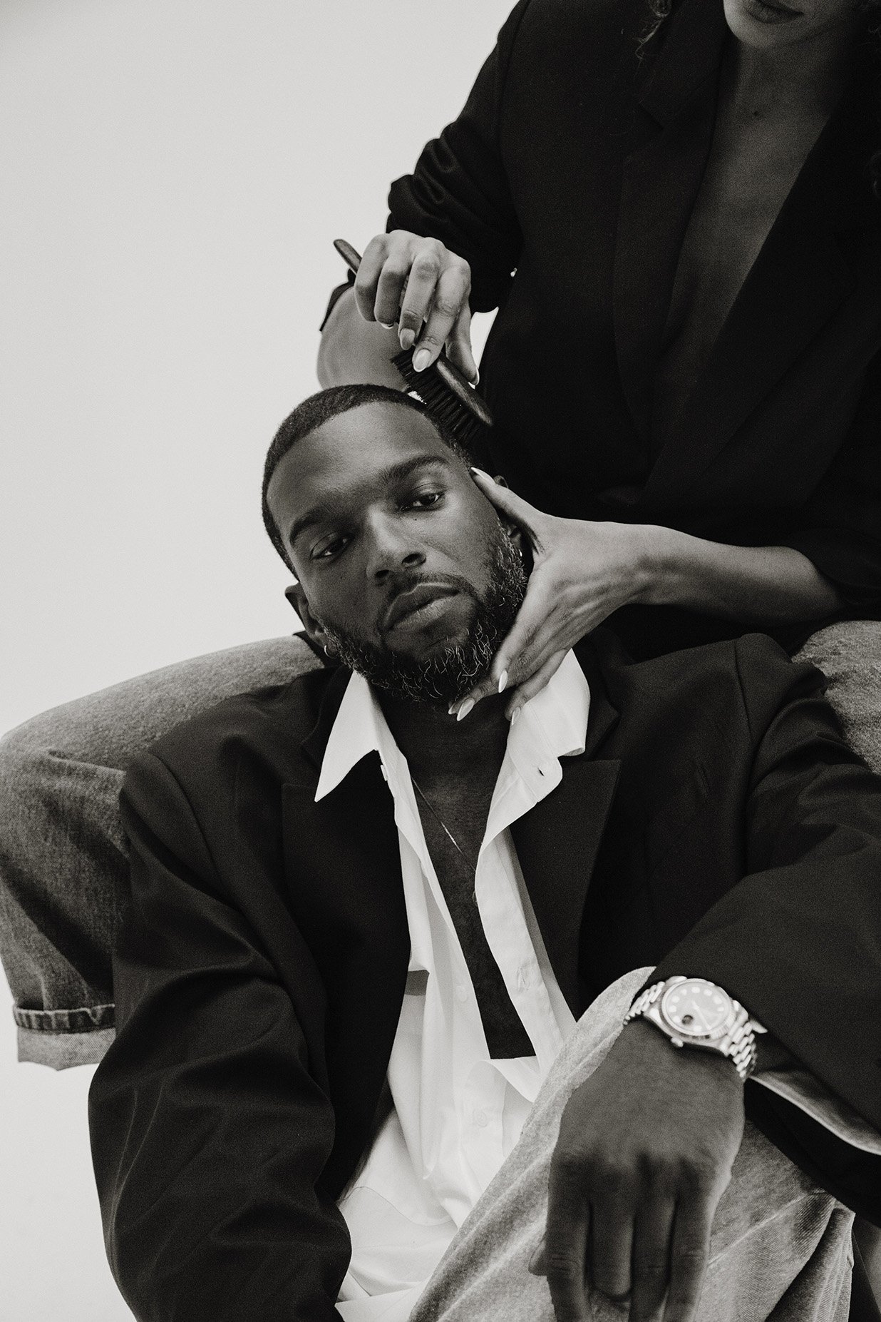 Monochrome portrait of a black man in a black blazer and white shirt with a stylist holding a comb