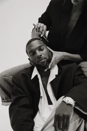 Monochrome portrait of a black man in a black blazer and white shirt with a stylist holding a comb