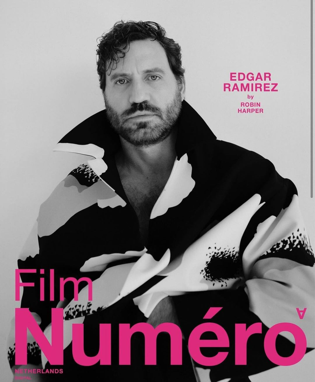Edgar Ramirez poses for a magazine cover, his photo is in black and white with a pink masthead. He wears a patterned jacket.