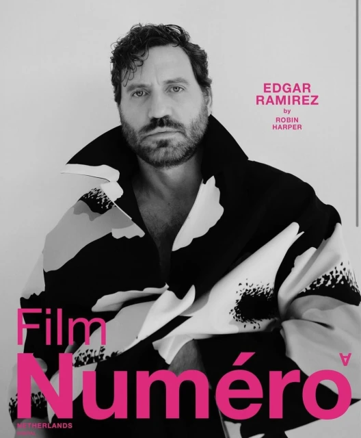 Edgar Ramirez poses for a magazine cover, his photo is in black and white with a pink masthead. He wears a patterned jacket.