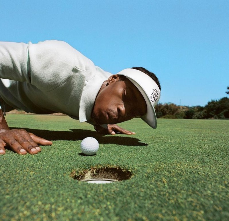 Golfer in visor peers closely at a golf ball on the green near the hole on a clear day, set on a lush green golf course.