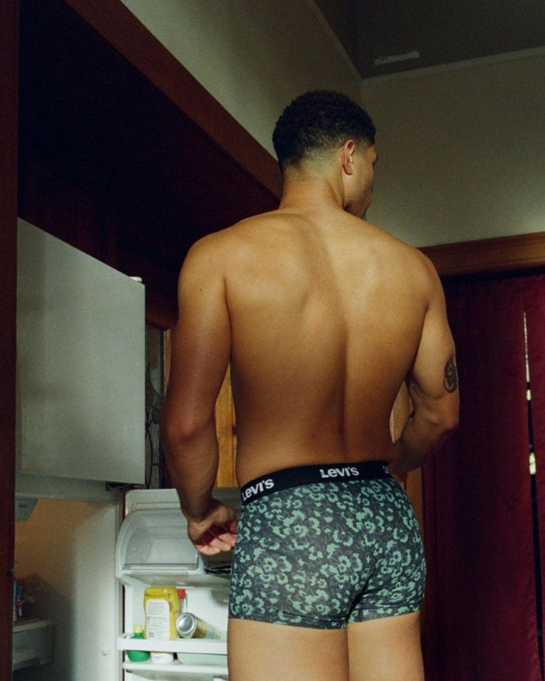 Shirtless man standing in a kitchen wearing printed briefs with visible waistband branding