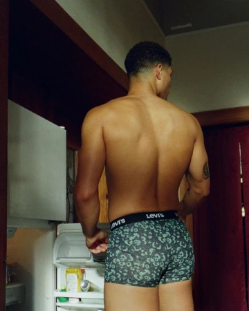 Shirtless man standing in a kitchen wearing printed briefs with visible waistband branding