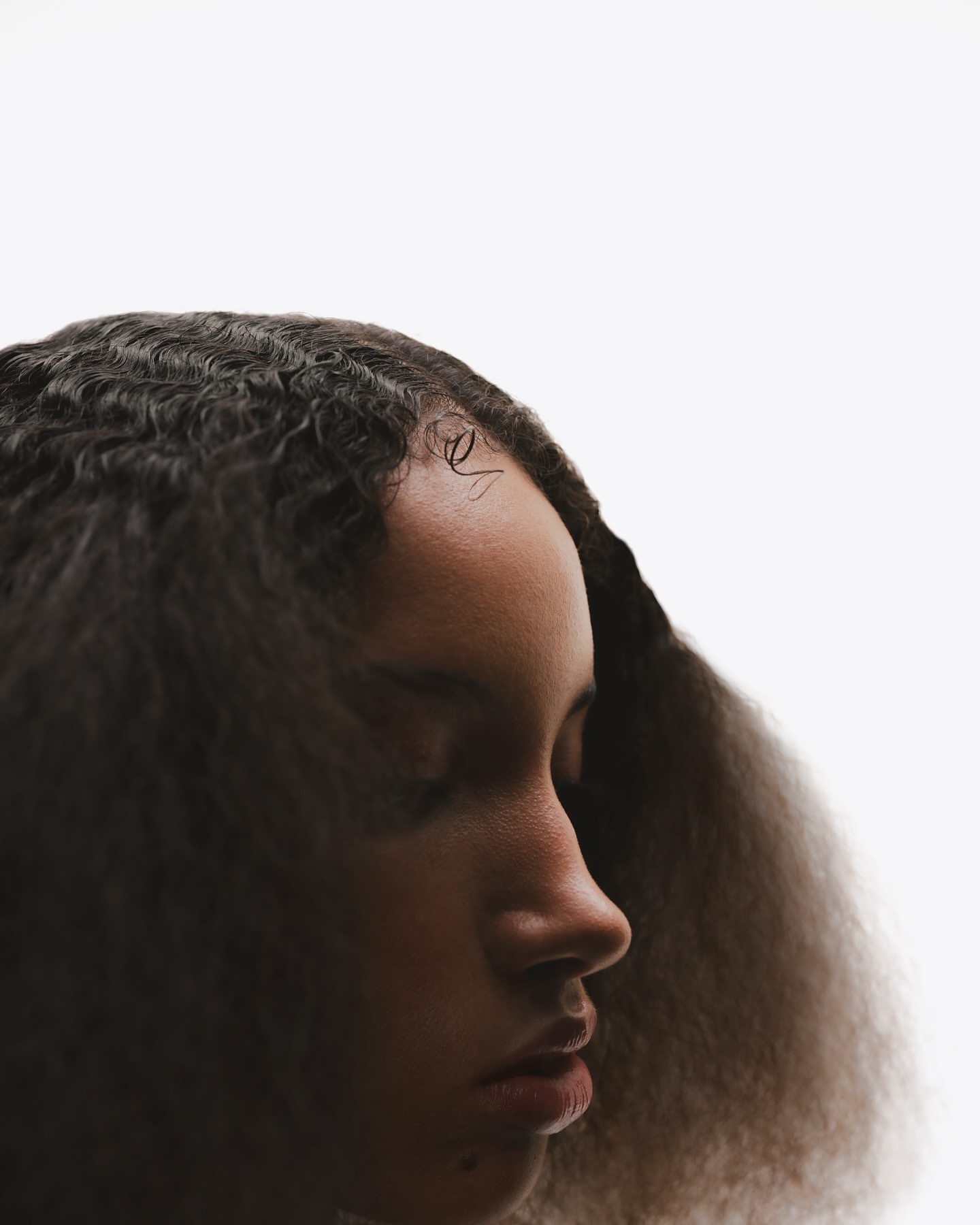Close-up portrait of a Black young adult woman in profile with curly dark hair against a white background, showcasing beauty and simplicity.