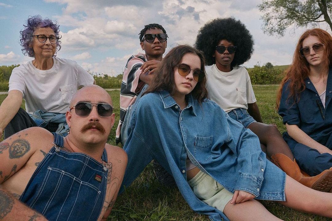 Group of six diverse people sitting outdoors on grass wearing casual denim and white t-shirts photographed by Robin Harper