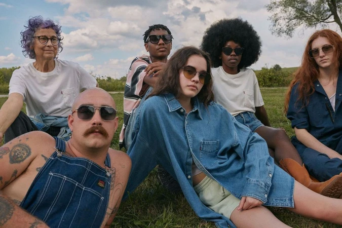 Group of six diverse people sitting outdoors on grass wearing casual denim and white t-shirts photographed by Robin Harper