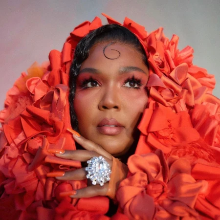 Close-up studio portrait of a woman with dark hair and a large diamond ring wearing an elaborate red floral garment around her head.