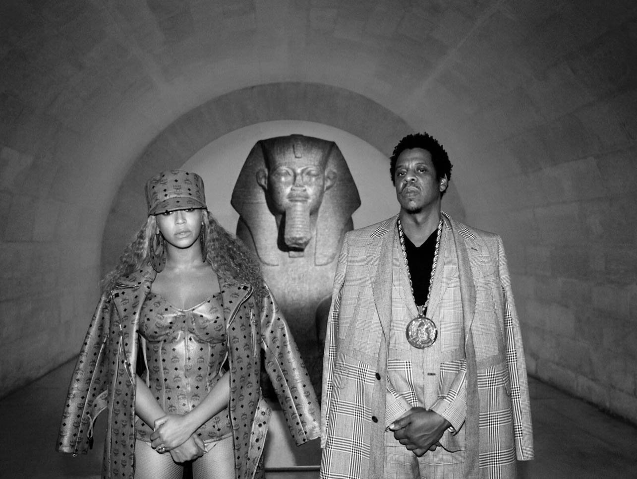 Monochrome portrait of Beyonc
Wilde and Jay-Z in patterned outfits, posing next to a stone Egyptian-style sculpture indoors.