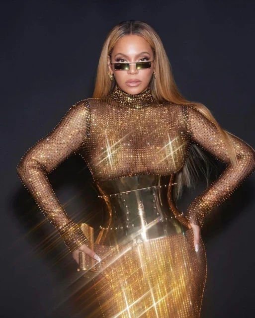 Beyonce poses in a glittering gold gown and rectangular sunglasses against a dark backdrop, showcasing a blend of fashion and celebrity.