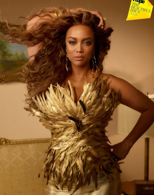 Tyra Banks is wearing a gold feathered dress on People Magazine's The Beautiful Issue, styled with gold jewelry, and soft brown wavy hair.