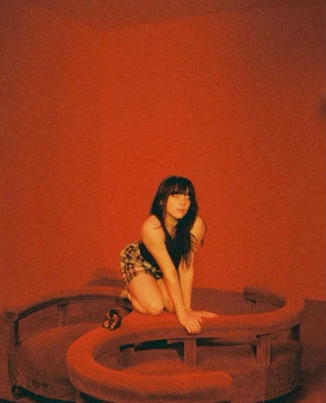 Young woman with dark hair kneeling on a curved red sofa inside a monochromatic red room shot by Robin Harper