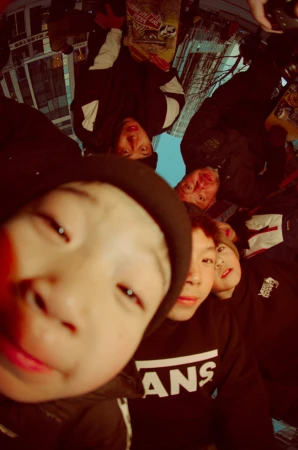 Low angle view of a group of Asian people including an Asian child in a black hooded jacket and a skateboard in an urban environment.