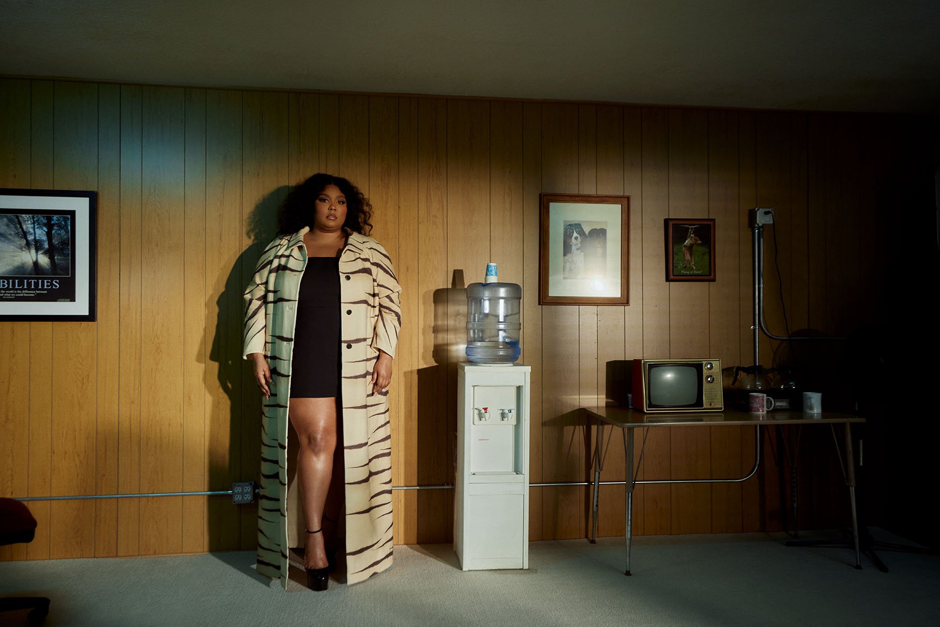An African-American woman poses in a modern tiger-striped coat and short black dress, standing in a room with vintage decor.