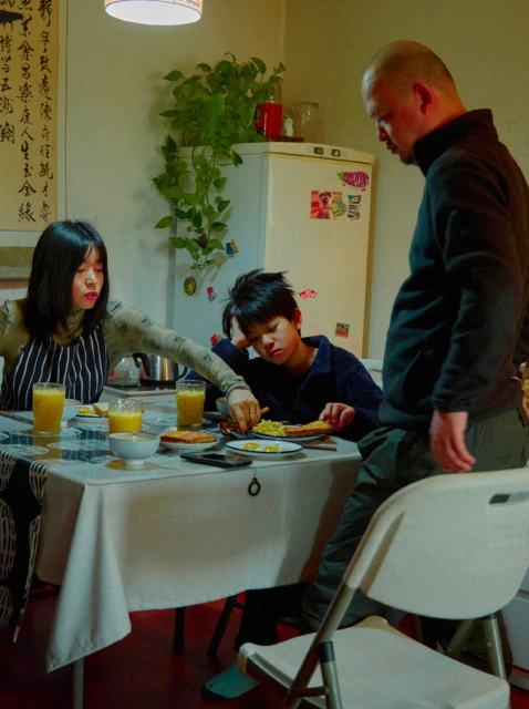 Family gathering around a table with food and drinks in an indoor setting. Adults and child are present in the scene.