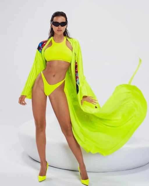 Model in a vibrant neon-yellow bikini and matching robe posing in front of a bright white backdrop in a fashion photography studio.