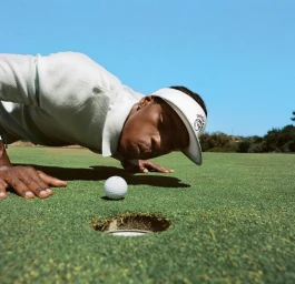 Man wearing a white visor doing pushups on a golf course near a golf hole and ball, photographed by Robin Harper.