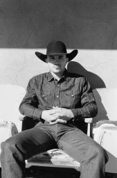 Man wearing a cowboy hat and denim shirt seated outdoors in Los Angeles, photographed by Robin Harper in monochrome.