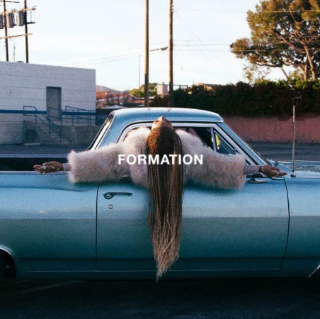 Beyonce with long braids lying across the roof of a vintage light blue car