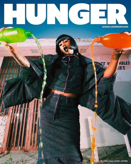 Hunger magazine cover featuring Flo Milli with two bottles of liquid that is pouring out in front of a building with signage.