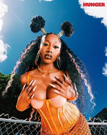 Low-angle portrait of a Black woman with styled hair buns wearing an orange corset top against a blue sky with clouds.
