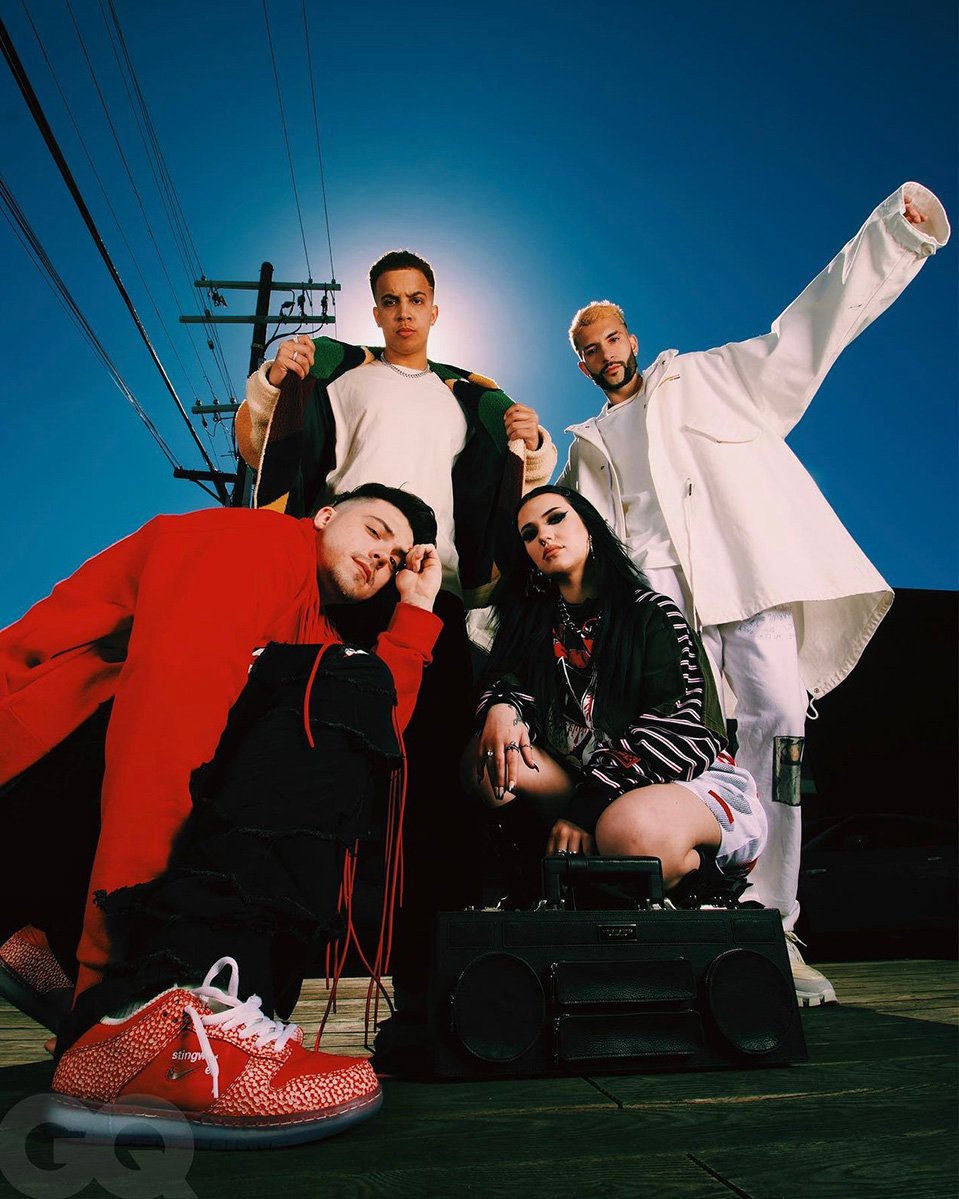 Four people pose outdoors at eye-level on a sunny day with an old-fashioned boombox. Streetlights and a blue sky in the background.