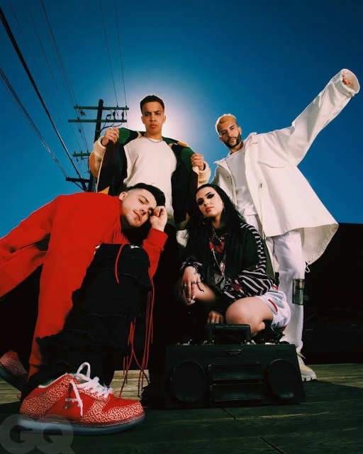 Four people pose outdoors at eye-level on a sunny day with an old-fashioned boombox. Streetlights and a blue sky in the background.