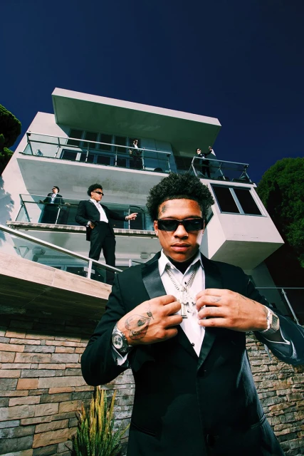 Stylish group portrait of a man in a black suit in front of a modern building with others in suits, against a blue sky backdrop.