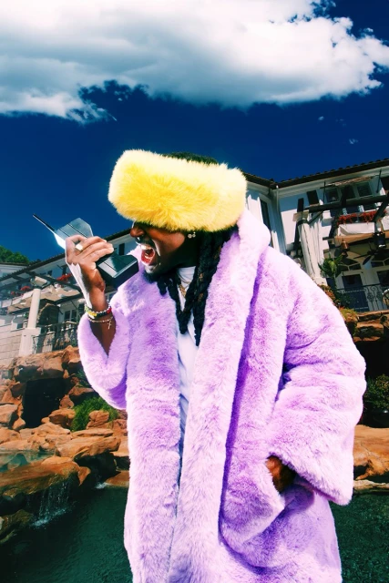 Stylish man in a yellow hat and purple coat talks on a retro telephone against a backdrop of a modern house and blue sky.
