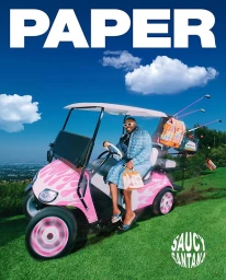 A Black man seated in a pink and white custom golf cart on a grassy hill under a bright blue sky with fluffy white clouds.