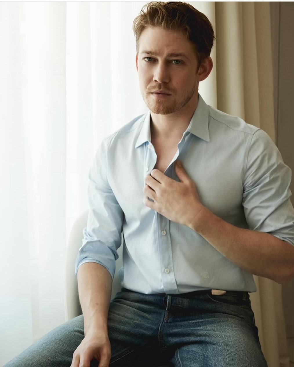 Portrait of a light-haired man in blue button-down shirt and jeans, indoors, gazing forward with natural expression and soft window light.