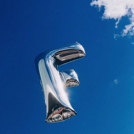 Silver letter F balloon against a bright blue sky with a few small clouds, creating a simple, celebratory, and visually striking composition.