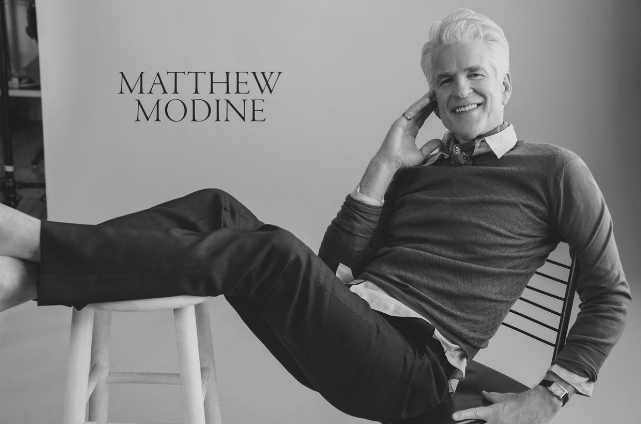 Portrait of actor Matthew Modine smiling with feet propped up on a stool, photographed by Victoria Stevens.