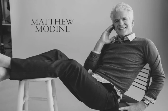 Portrait of actor Matthew Modine smiling with feet propped up on a stool, photographed by Victoria Stevens.