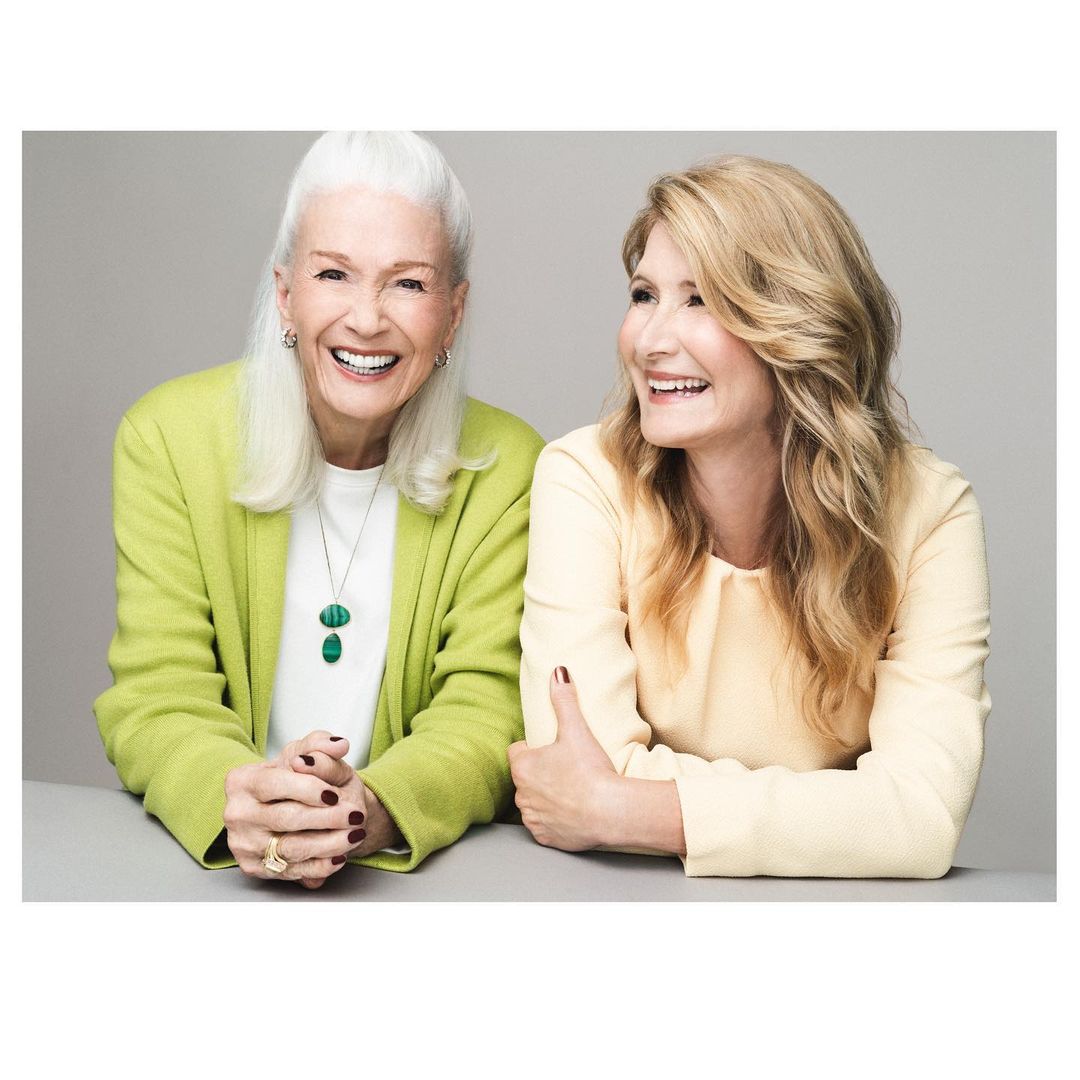 Portrait of two smiling women, one elderly with white hair in a green jacket and one younger with blonde hair in a yellow blouse.