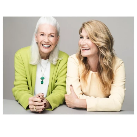 Portrait of two smiling women, one elderly with white hair in a green jacket and one younger with blonde hair in a yellow blouse.