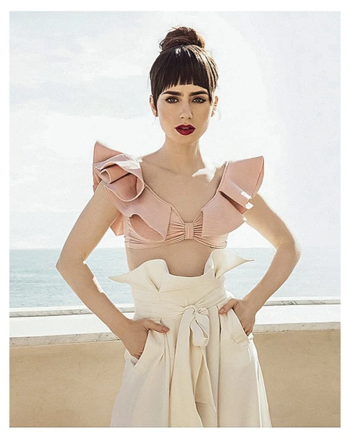 Fashion portrait of a stylish adult woman with an elaborate top and pants posing outdoors on a sunny day with the sea in the background.