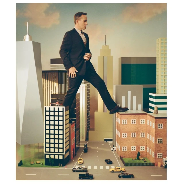 Businessman steps from toy skyscraper over miniature city street, with toy cars and pedestrians, against a blue sky backdrop.
