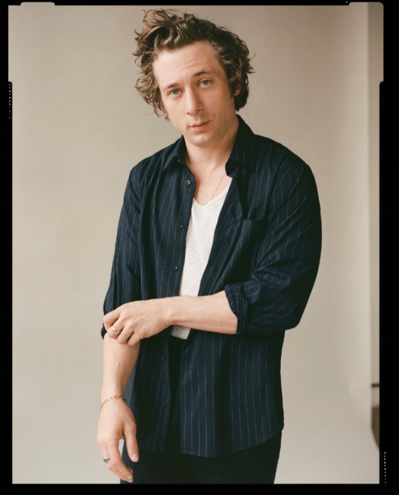 Portrait of a young adult male with curly brown hair wearing a striped shirt and white undershirt against a neutral backdrop.