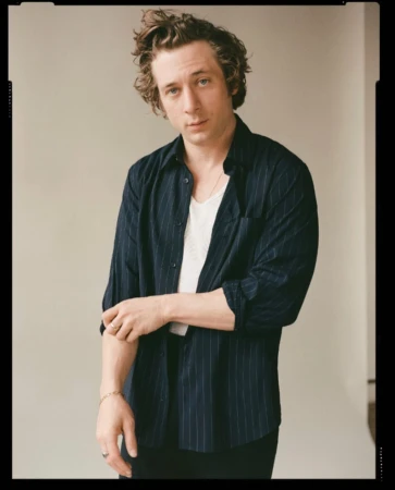 Portrait of a young adult male with curly brown hair wearing a striped shirt and white undershirt against a neutral backdrop.