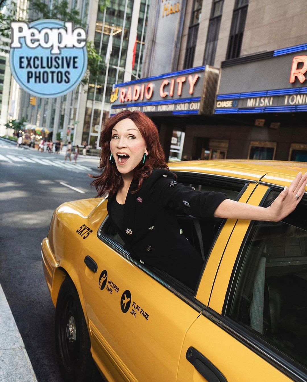 Patricia Heaton exits a yellow taxi in an urban environment, dressed in a black jacket and smiling; Radio City Music Hall is visible in the background.